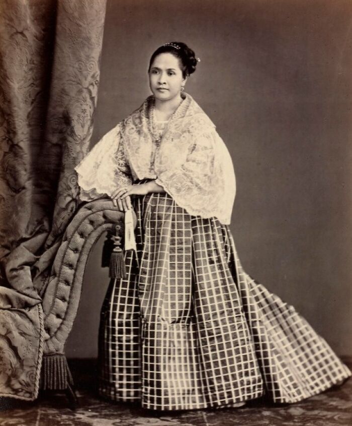 Filipina woman in traditional 1890s attire standing beside an ornate curtain, showcasing Philippines culture and history.