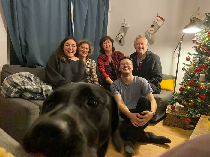 Family smiling on couch with dog photobombing close to the camera in a funny pets crashing photos moment.