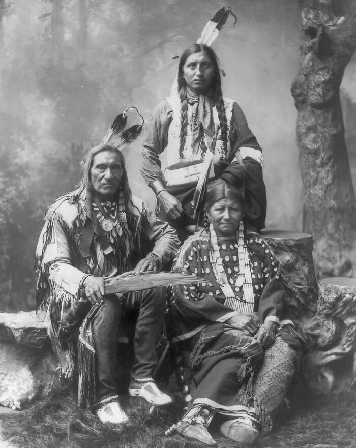 Vintage Native American family posed in traditional clothing with feather accessories in a historic black and white photo.