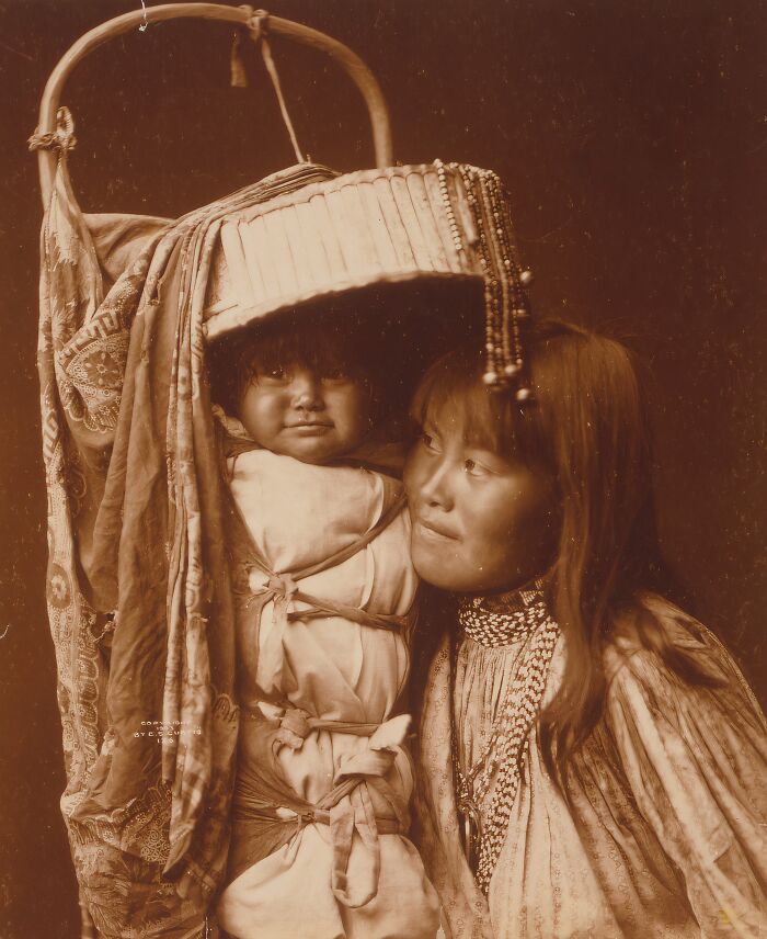Vintage Native American family photo of a mother carrying her child wrapped in traditional cloth and basket carrier.