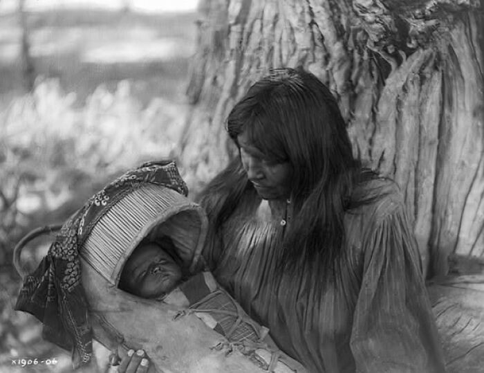 Native American mother holding her baby in a vintage family photo with traditional clothing and a woven cradleboard.