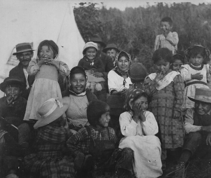 Vintage Native American family photo showing multiple generations of children and adults outdoors by a tent.