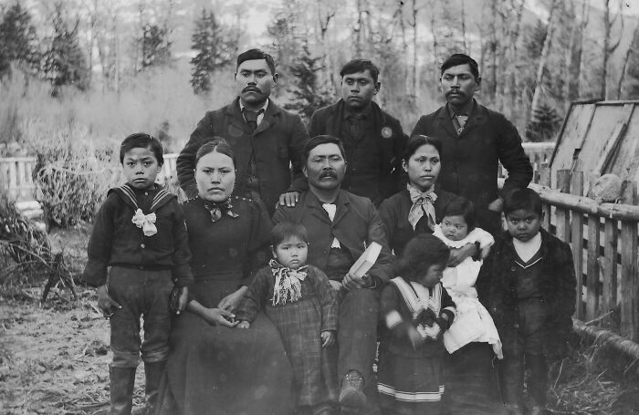 Vintage Native American family portrait outdoors, showing multiple generations dressed in early 20th century clothing.