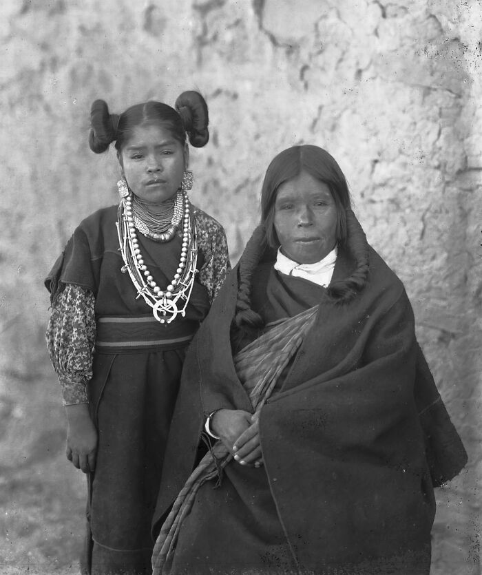 Vintage Native American family portrait with a mother and daughter dressed in traditional clothing and jewelry.