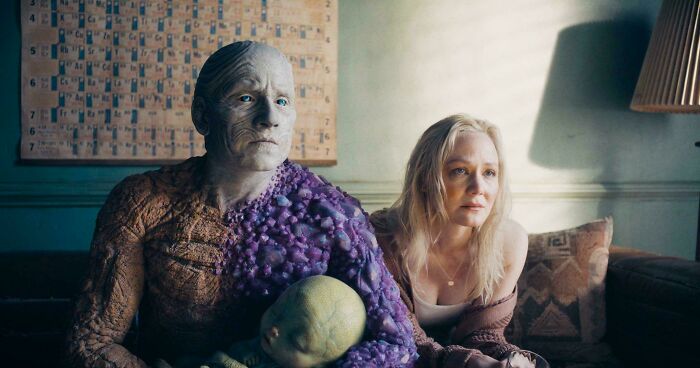 Character with detailed makeup sitting next to a woman in a dimly lit room, highlighting bad movie details and confusing scenes.