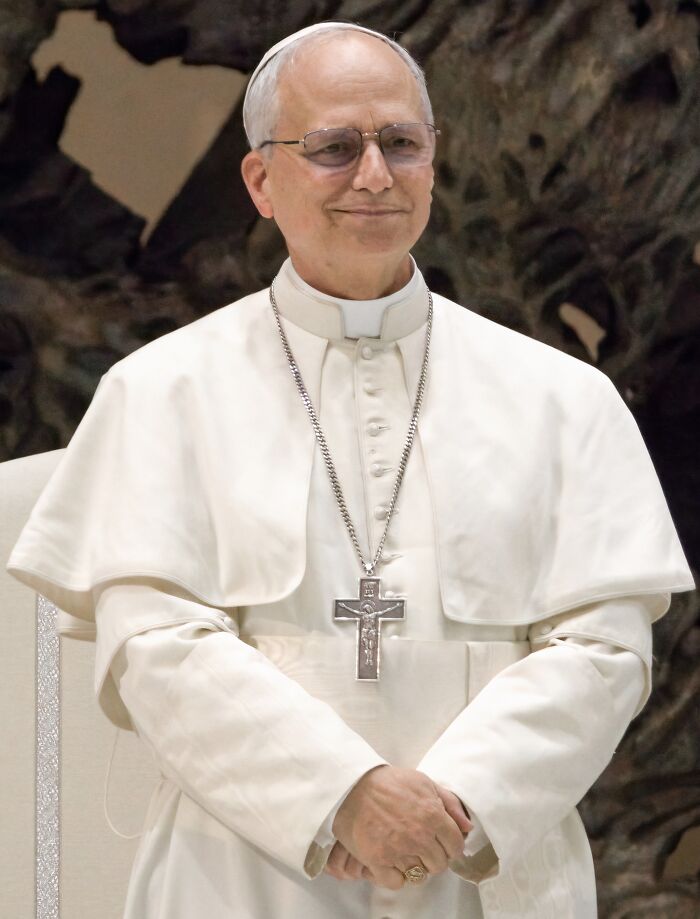 Religious leader in white robes wearing glasses and a silver cross necklace featured in headlines that rocked the world in 2025.