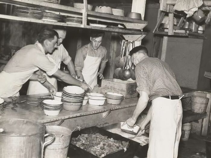Four men in aprons preparing food in a kitchen with bowls and large pots during the Great Depression era.