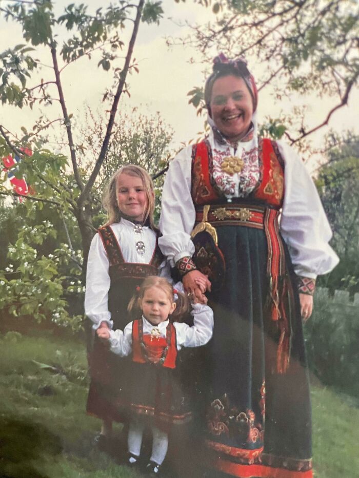 Three generations wearing traditional dresses standing outdoors in nature, a comparison of cultural heritage and family bonds.