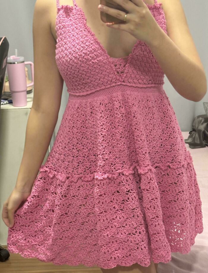 Woman wearing a pink crocheted dress showcasing detailed crochet patterns in a casual indoor setting.