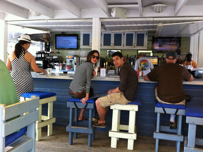 Group of people sitting at a casual beach bar, capturing vacation pics with funny and candid moments in a relaxed setting.
