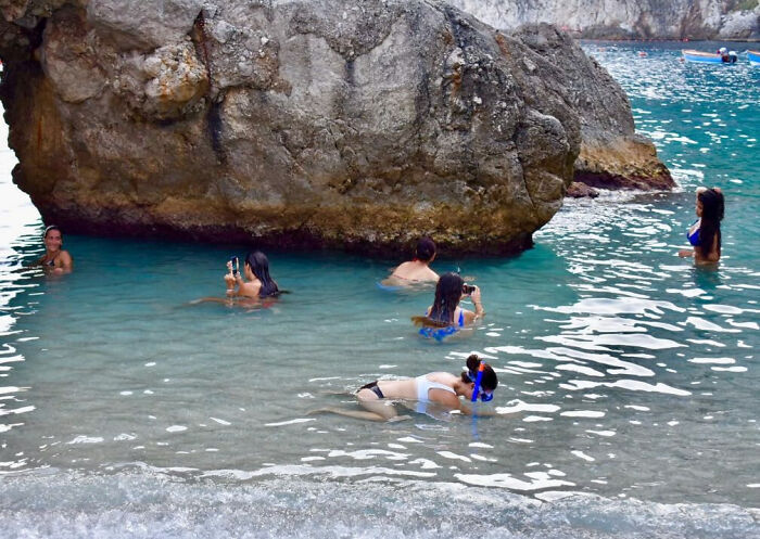 People taking vacation pics underwater near a large rock in clear blue water, capturing unique moments humorously.