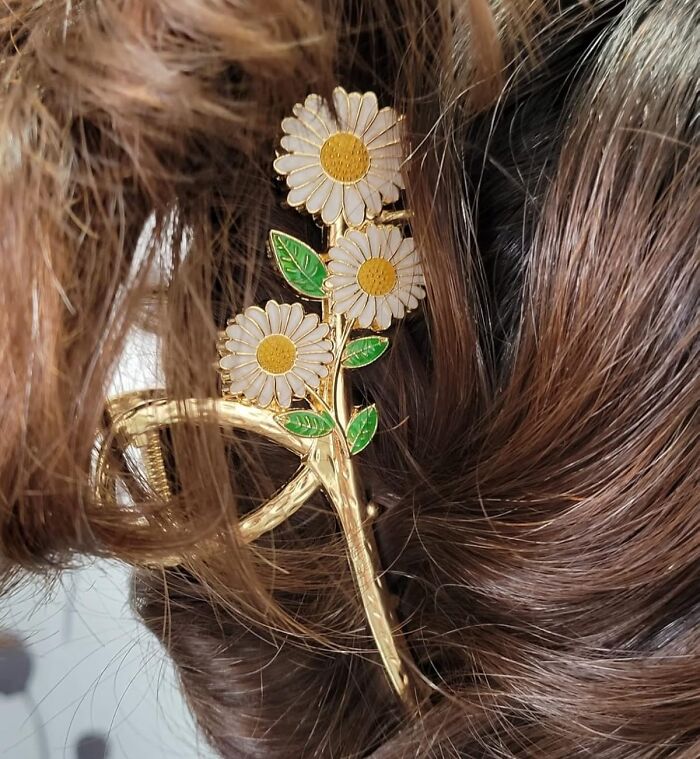 Gold hair clip with white and yellow daisies and green leaves securing brown hair, showcasing fun and functional accessory design.