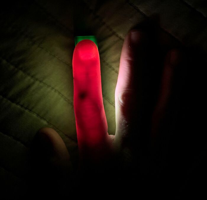 Finger illuminated in red light showing veins and bone structure, illustrating a fascinating extra finger on a human hand.