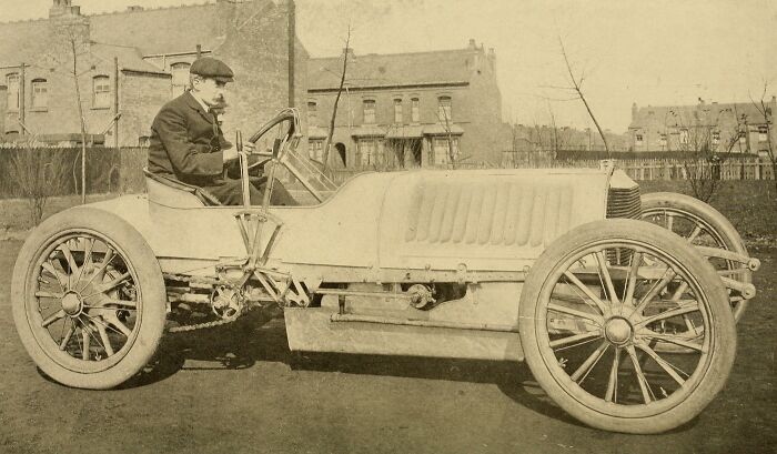 Early vintage car with large spoked wheels and a man driving, showcasing how wild the first cars really were 100 years ago.