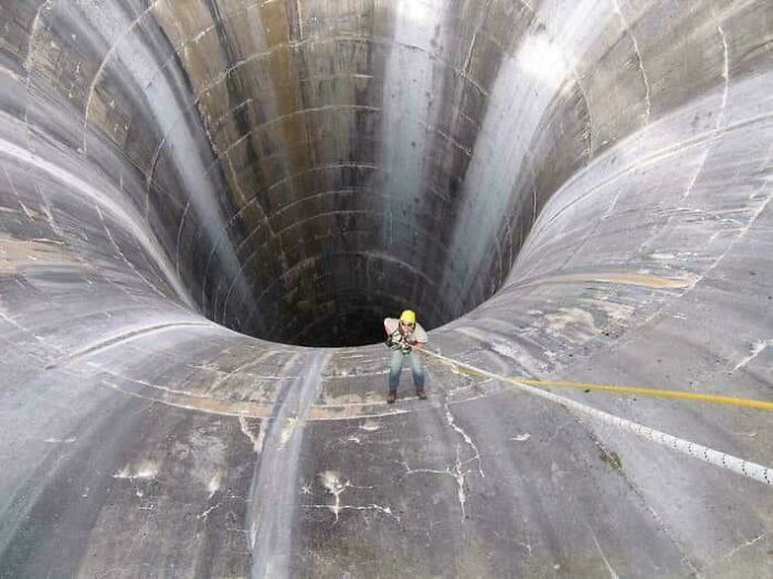 A person rappelling into an extremely large, scary, and eerie concrete dam spillway.