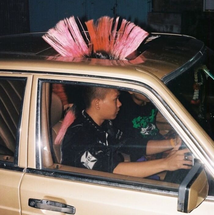 Two people inside a car, one with a pink mohawk hairstyle, an example of cursed images from a popular IG page.