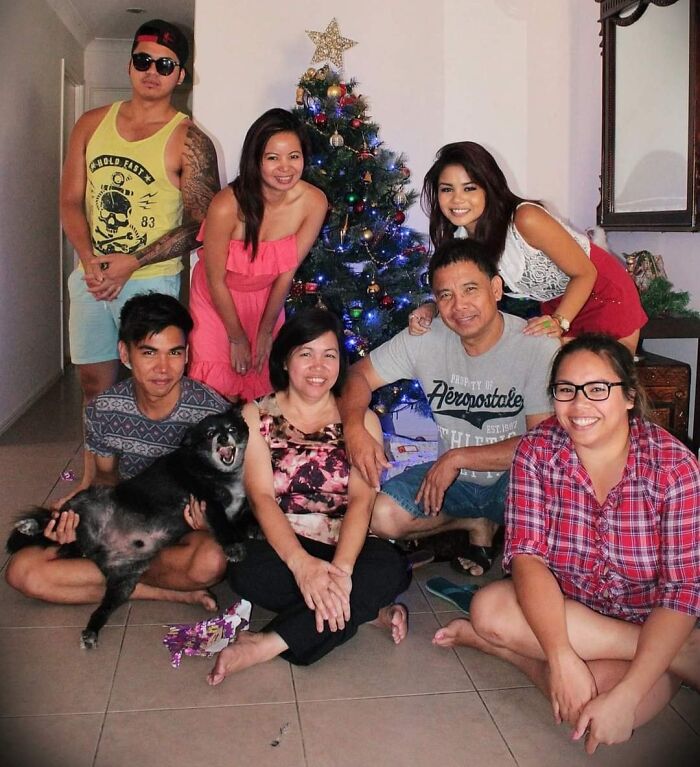 Group photo near Christmas tree with a black dog crashing the picture, showcasing funny times pets stole the show.