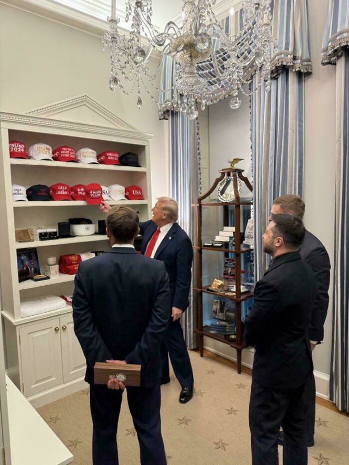 Donald Trump and three men in suits viewing a collection of red and white hats in an ornate room, universe had different plans.