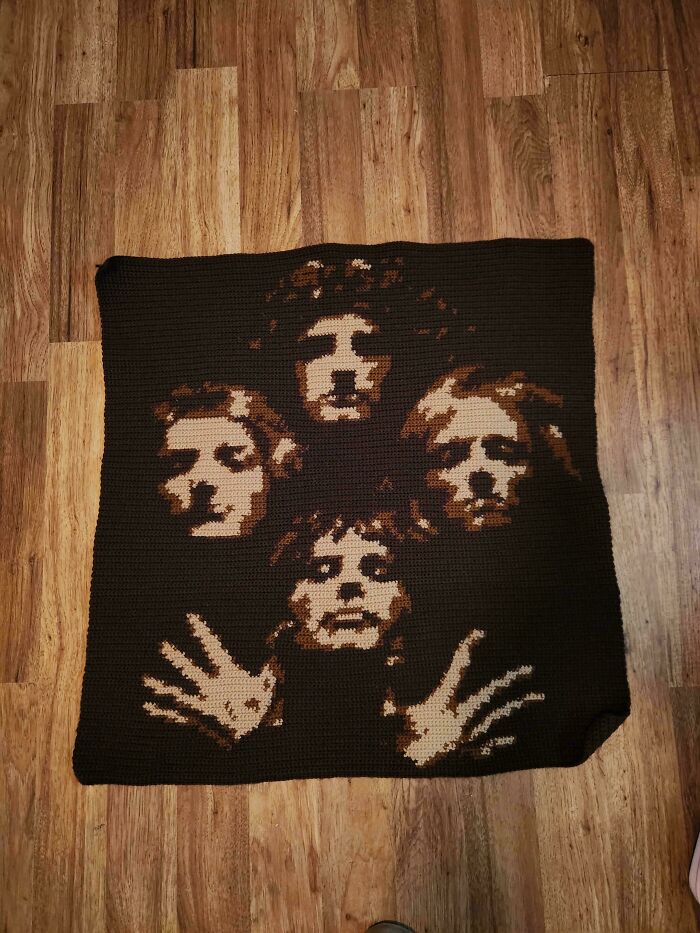 Crocheted blanket depicting a detailed portrait of four faces and hands on a wooden floor background.