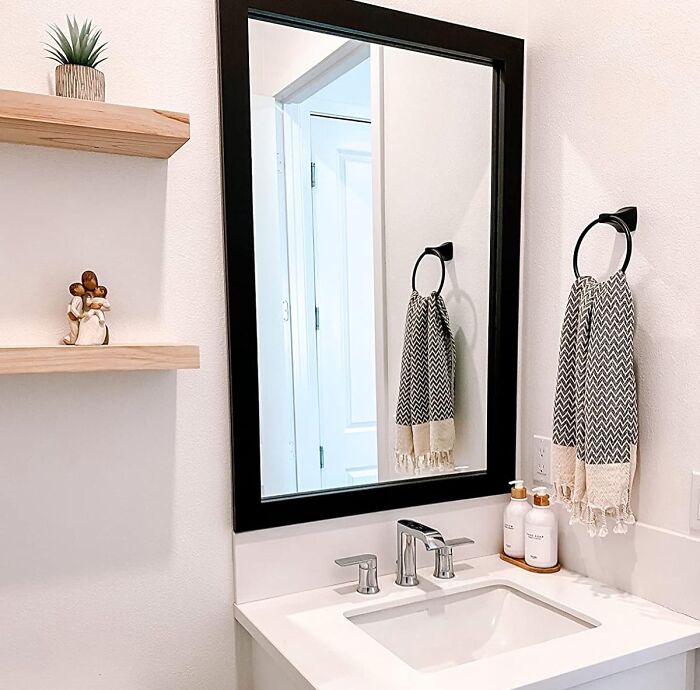 Modern bathroom sink with chrome faucet, black-framed mirror, patterned hand towel, and minimalist shelf decor.