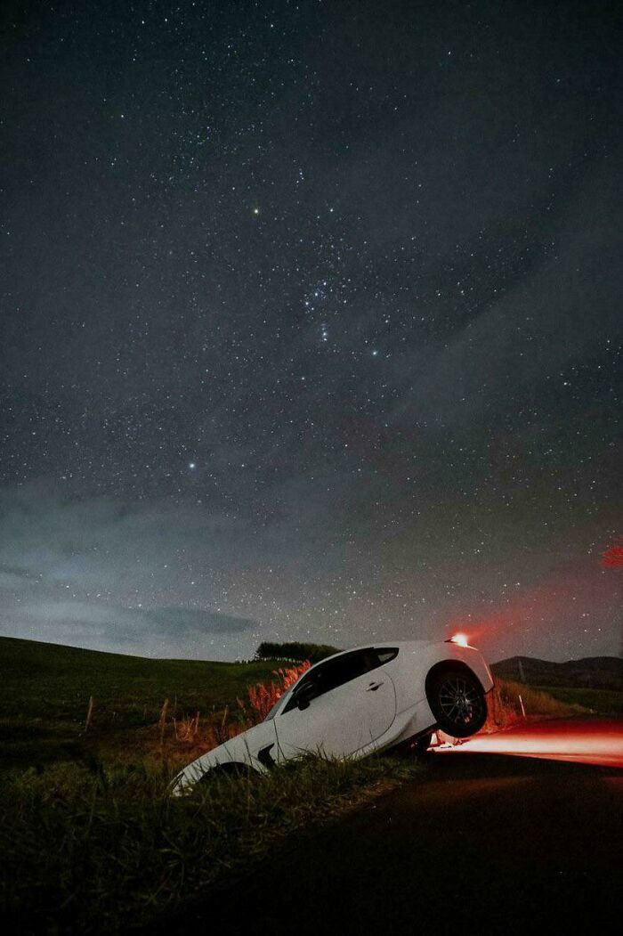 White car stuck at the edge of a roadside ditch at night under a starry sky, showing a clear parking fail.