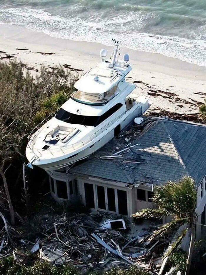 A large yacht crash-parked on the roof of a damaged beach house, illustrating a major parking fail.