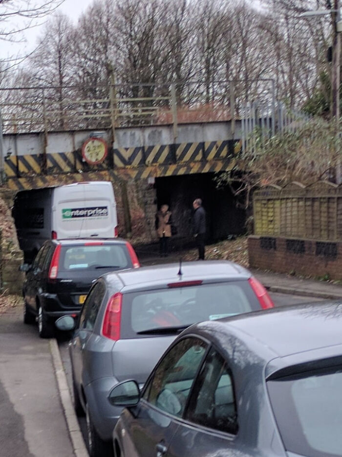 Several cars parked closely along a narrow street near a low clearance bridge, illustrating parking fails.