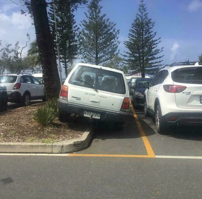 Small white car parked incorrectly on a curb next to other vehicles showing a clear parking fail.