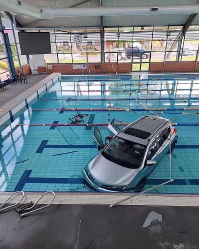 Silver car submerged in an indoor swimming pool showing a major parking fail causing damage and disruption.