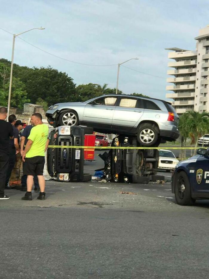 Silver car parked on top of two overturned vehicles at an accident scene with police and onlookers nearby parking fails