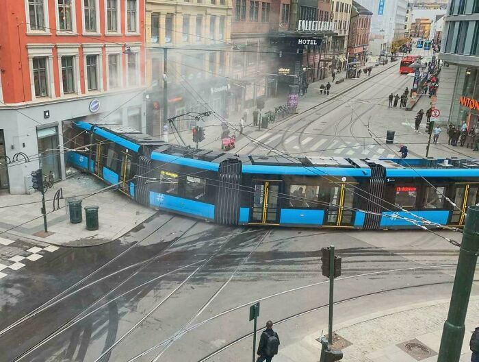 Blue tram crashed into building on city street, highlighting a major parking fail in urban area with pedestrians nearby.
