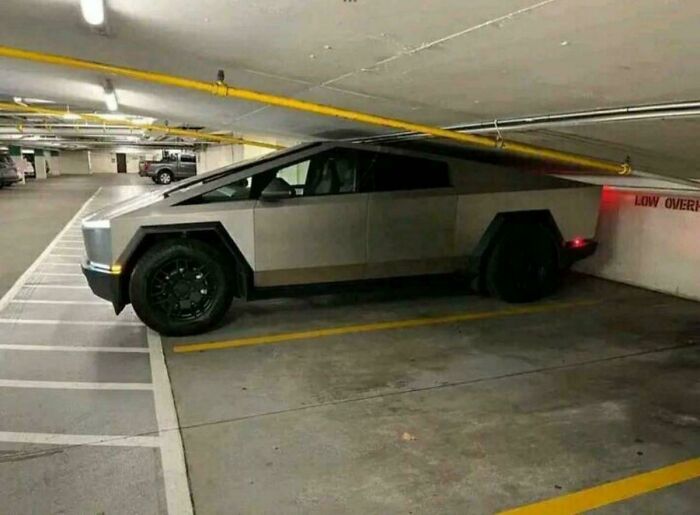Electric truck parked in a low clearance garage with the roof of the vehicle stuck under a yellow pipe, a parking fail.