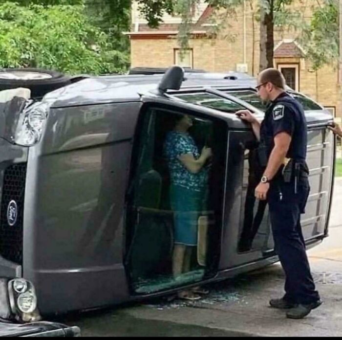 Police officer talking to a person inside a flipped car after a major parking fail incident on a residential street.