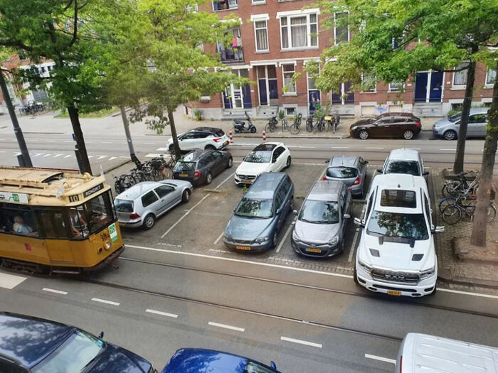 Cars and a tram sharing a narrow street space, illustrating a parking fail in an urban setting with trees and bikes nearby.