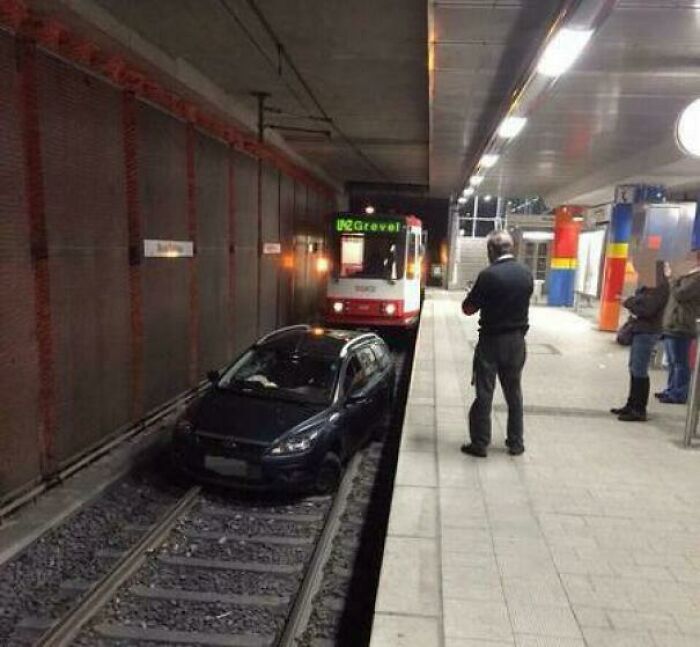 Car parked on train tracks at a station platform causing a major parking fail and blocking an arriving train.