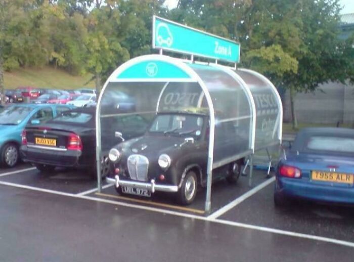 Vintage car parked in a cart shelter causing a parking fail in a busy outdoor parking lot with other vehicles nearby.