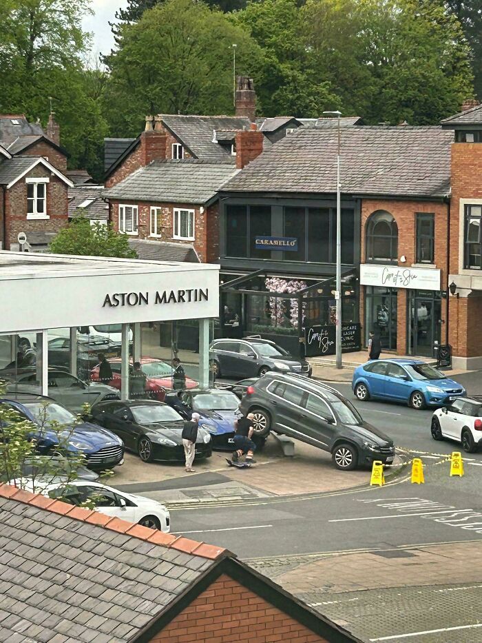 Car parked on top of another vehicle outside Aston Martin dealership, showcasing a major parking fail caught online.