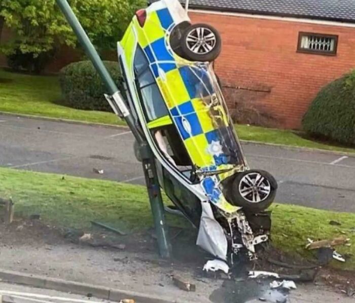 Police car crashed and stuck vertically against a lamp post in a parking fail captured on the roadside.