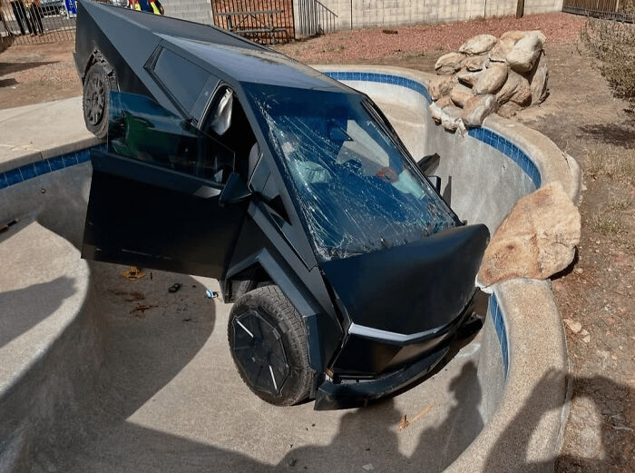 Black futuristic truck crashed into an empty pool, showing a major parking fail with shattered windshield and open door.
