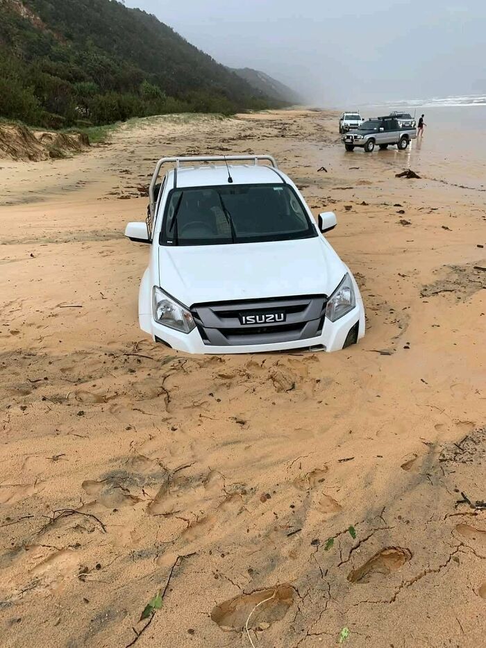 White Isuzu stuck in deep sand on a beach illustrating one of many parking fails shared online.