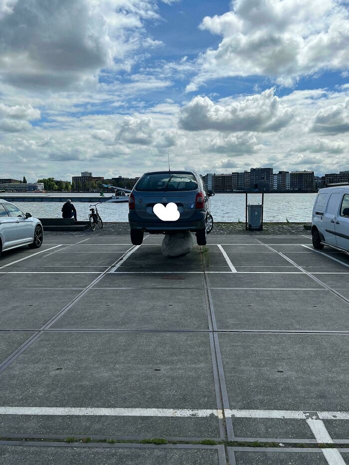 Car lifted on a rock in a parking spot by the waterfront, illustrating a parking fail shared online.