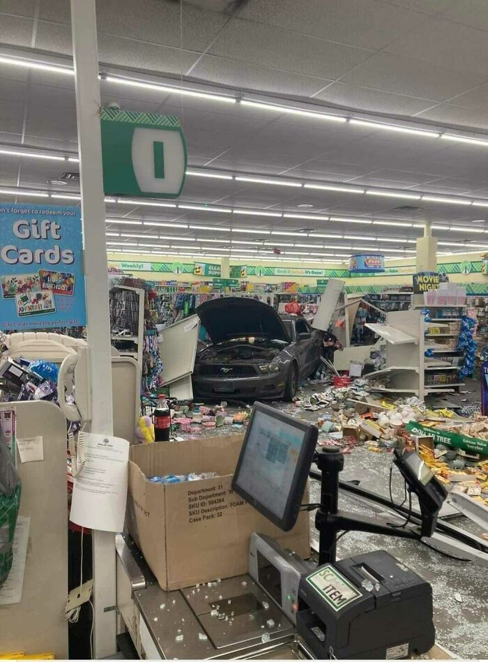 Car crashed into store aisle causing a major parking fail with broken shelves and scattered products inside the shop.