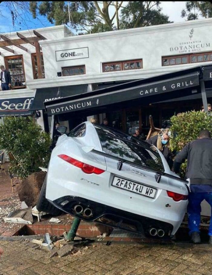 White sports car crashed into sidewalk and garden, illustrating a severe parking fail outside a café and grill.