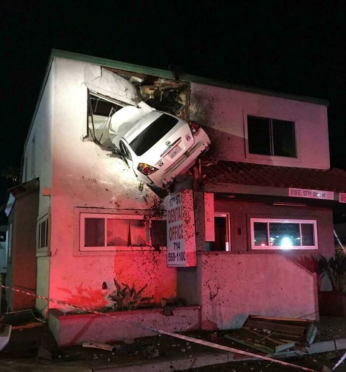 White car crashed into second-story wall of building at night, showcasing one of the most extreme parking fails captured online.