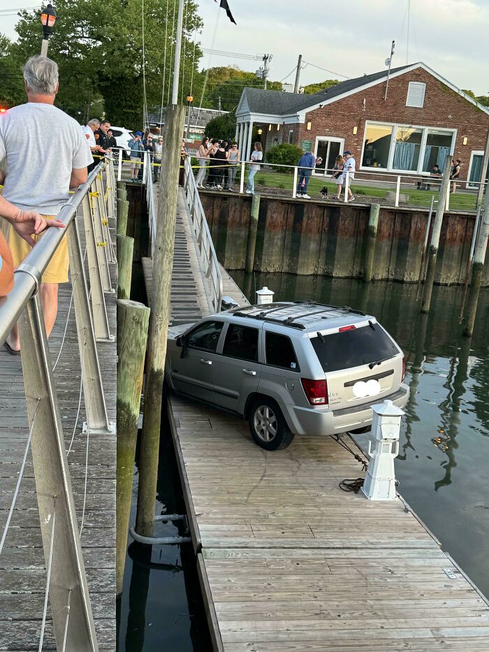 Silver SUV parked on a narrow dock by the water with onlookers nearby in a clear example of parking fails.