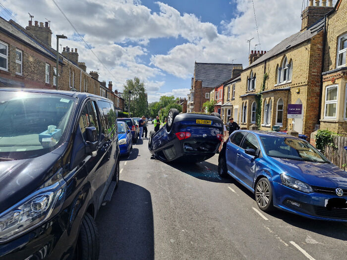 Car flipped upside down on a residential street, surrounded by parked cars, representing one of many parking fails shared online.