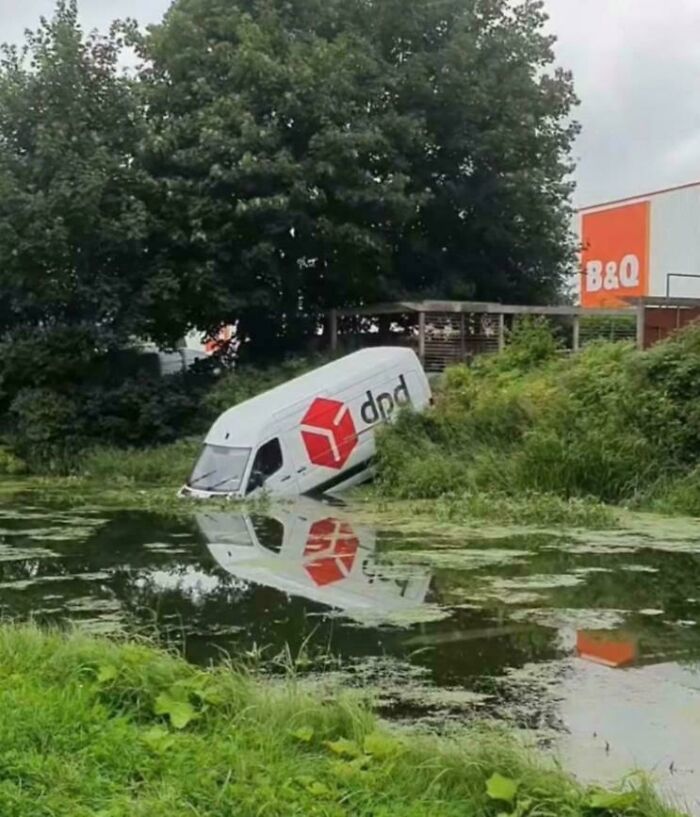 Delivery van partially submerged in a pond after a parking fail near a B&Q store surrounded by greenery.