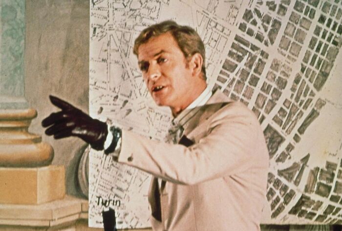 Actor dressed in vintage attire with black gloves pointing and standing in front of a large detailed city map iconic heartthrobs photo.