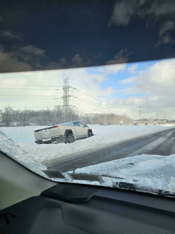 Silver electric truck stuck in snow on roadside during winter, showcasing a notable parking fail in snowy conditions.