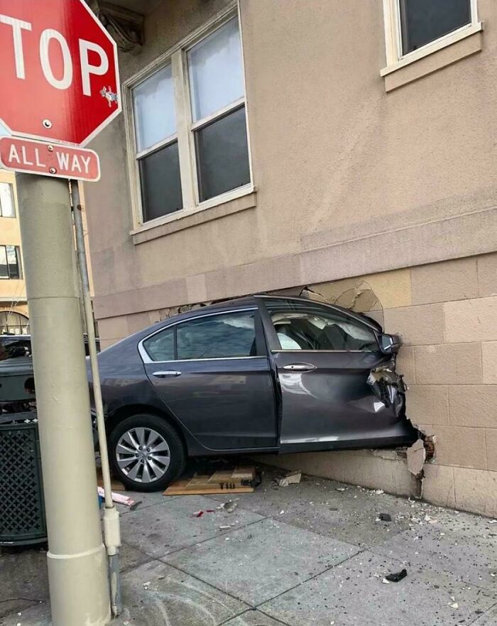 Car crashed into a building wall, illustrating a severe parking fail on a city sidewalk near a stop sign.